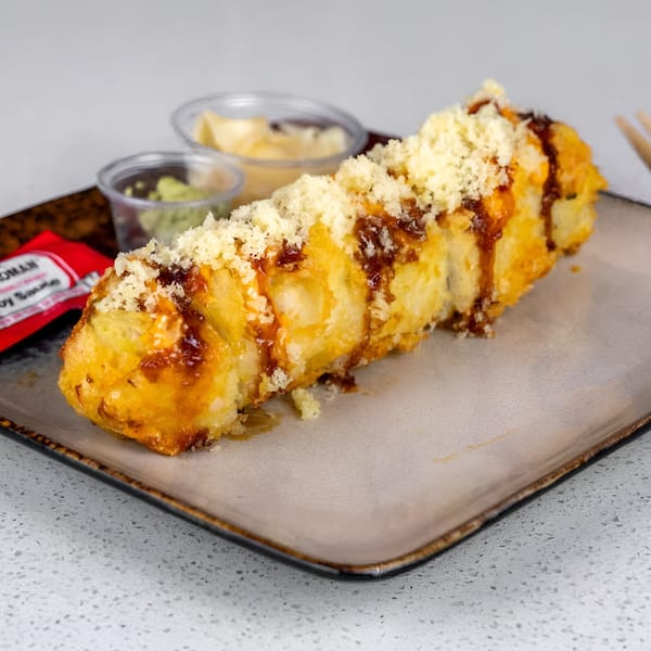 Deep-fried sushi roll drizzled with sauce and topped with crunchy flakes, served with soy sauce and wasabi.