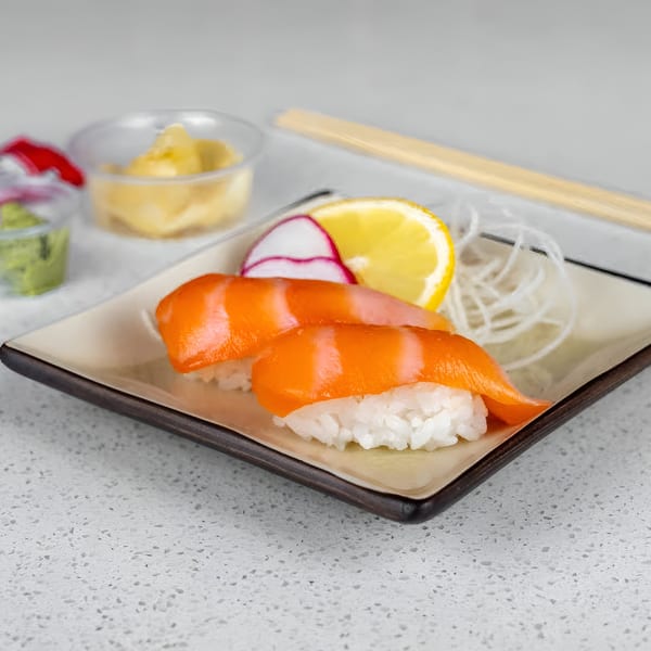 Two pieces of salmon nigiri sushi with lemon, radish, and shredded daikon on a plate.