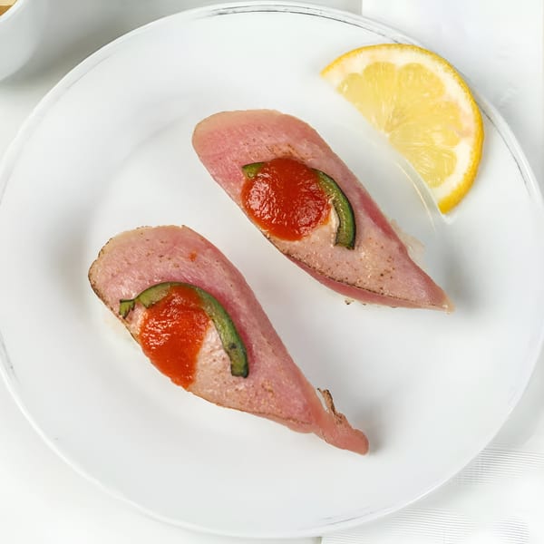 Two pieces of Sushi Totoro's seared tuna nigiri with red sauce, green pepper, and a lemon wedge.